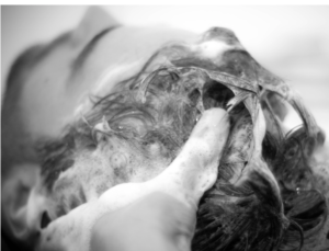 A hand with soap suds shampooing a man's hair from the back.